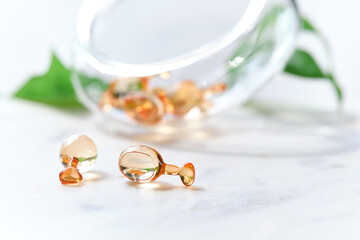Serum capsules for healthy skin. Blurred background, glass jar with the capsules and green leaf.