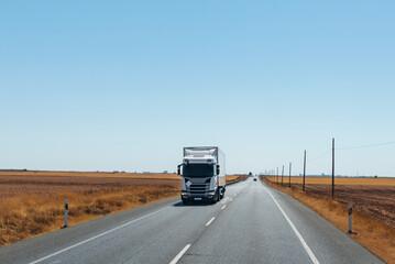 Refrigerator truck driving on a straight road, with a flat horizon and a clear sky.