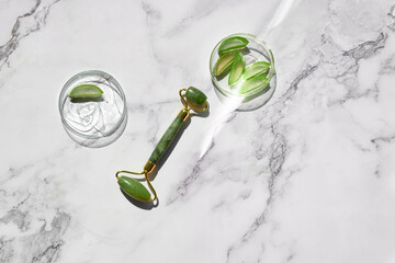 Aloe vera home made moisturizer and green jade face roller on off white marble background. Simple, minimal flat lay, top view. Facial massage concept, handmade cosmetics.