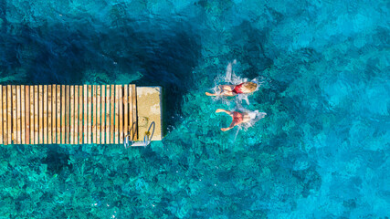 A carefree couple jumps into the azure sea. Aerial view. A vacation in the summertime. Young and energetic people dive into the water together. A fun vacation at the sea together. - Powered by Adobe