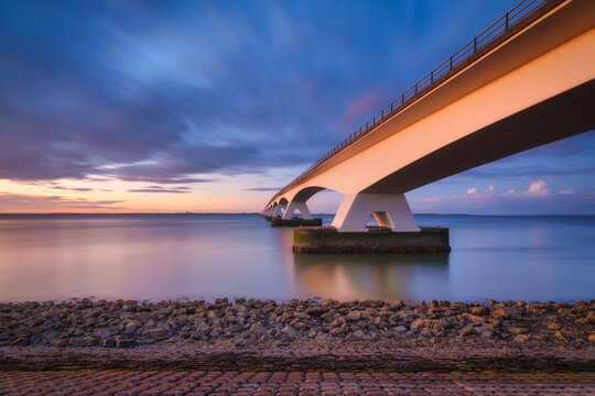A long bridge over the sea during sunset. Long exposure photo. Landscape during a bright sundown. The sea and the bridge. Zeeland bridge, Netherlands.