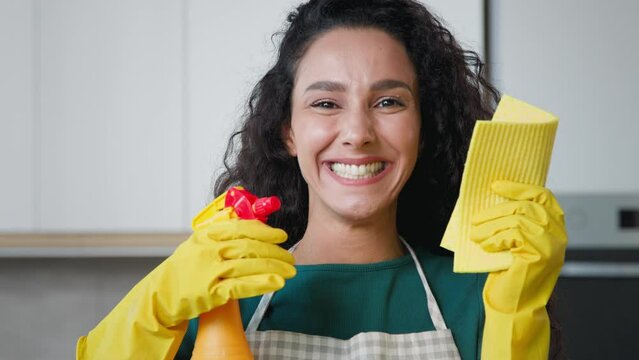 Happy young housewife mistress female maid worker housekeeper mother wife posing in kitchen wears yellow rubber protective gloves hold cleanser bottle spray detergent liquid on wet rag for cleaning