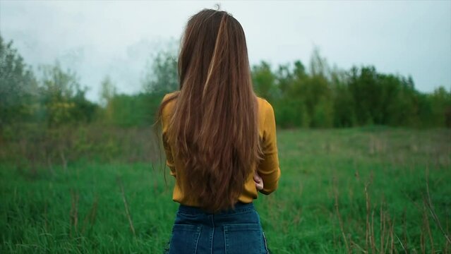 Girl with long hair in a yellow sweater stands with her back and smokes in nature