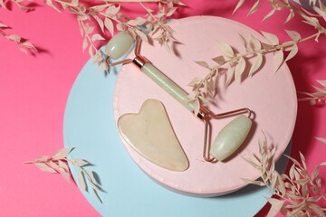 Flat lay composition with gua sha stone and face roller on pink background