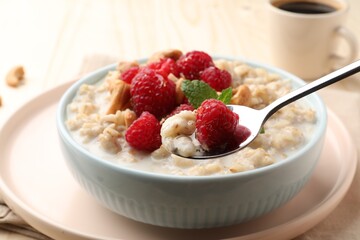Bowl with tasty oatmeal porridge with nuts and raspberries on table, closeup. Healthy meal