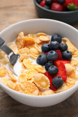Bowl of tasty crispy corn flakes with milk and berries on wooden table, closeup