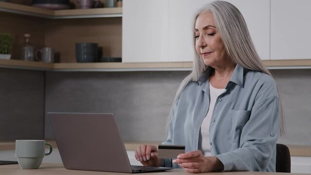 Elderly lady buyer grandmother shopper mature woman sit in kitchen pay utility bills on laptop use banking app for online charity enter security card number at computer internet financial transaction