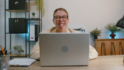 Business woman hiding behind laptop computer, making funny face, fooling around, putting his tongue...