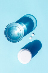 Pills and glass of water on blue background. Medicine, healthcare concept