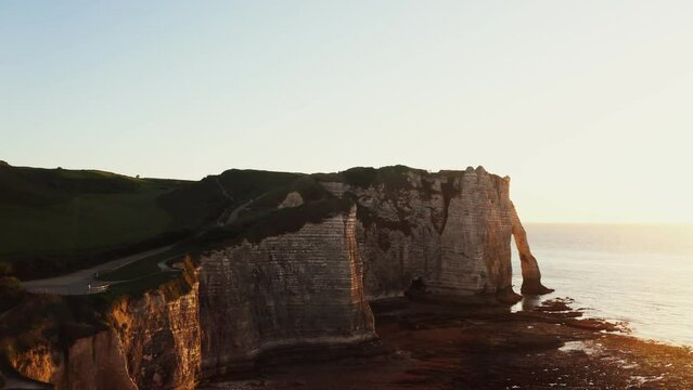 Picturesque sheer cliffs of limestone and flint with photogenic natural arches, washed by the waters of the English Channel in the red rays of the setting sun. Etretat, France