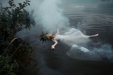 A lake nymph in a white dress and a wreath of flowers floats on the surface of the water. A young woman in a folk image, a mystical story - obrazy, fototapety, plakaty