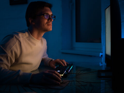 Programming and application development, a young man with glasses sits at a computer and is engaged in programming, code development, information technology.