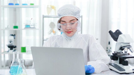 Portrait of beautiful asian woman wearing scientist suit uses laptop to analyze an experiment in special laboratorys