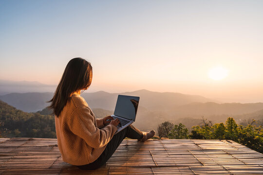 Young woman freelancer traveler working online using laptop and enjoying the beautiful nature landscape with mountain view at sunrise