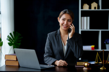 Lawyer concept. Beautiful Asian lawyer is talking on the phone with a client and using a laptop to...
