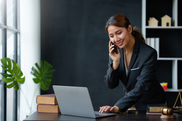 Lawyer concept. Beautiful Asian lawyer is talking on the phone with a client and using a laptop to...