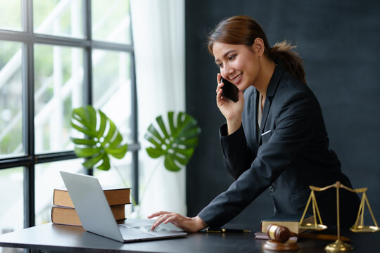 Lawyer Concept. Beautiful Asian Lawyer Is Talking On The Phone With A Client And Using A Laptop To Review Legal Matter To Support The Case File Consequences Of Legal Action On Client.