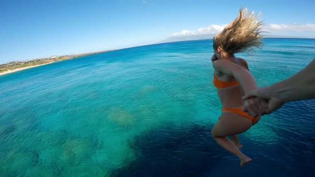 POV Couple holding hands cliff jumping into tropical ocean