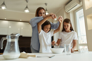 Happy family preparing food together in the kitchen. Mom teaches her daughters how to cook and knead the dough. Mother's Day concept. break eggs