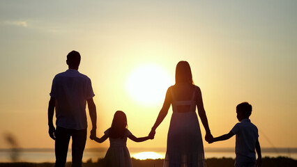 Fototapeta na wymiar Happy family looks at sunset standing on huge meadow. Mother and father silhouettes hold hands with kids looking at sunset against blue sky, closeup