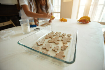 two little girls and their beautiful mother in aprons play and laugh, put gingerbread cookies in molds, on a baking sheet