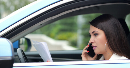 Serious businesswoman driver talks on smartphone with employee discussing papers. Woman discovers content of documents in traffic jam closeup