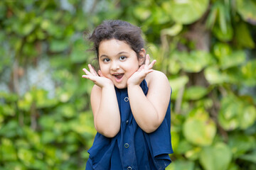 Fototapeta premium Happy cute little indian girl child with surprise expression on her face standing at park.
