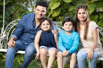 Happy young indian family pending time together while sitting on hanging swing.