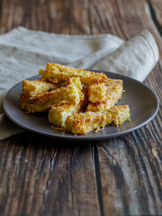 crunchy zucchini sticks breaded with breadcrumbs, parmesan cheese, spices on a black plate with grey napkin on a dark brown wooden table, side view close up vertical