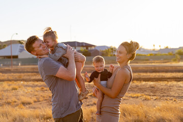 young parents with two young kids in golden light with houses in background