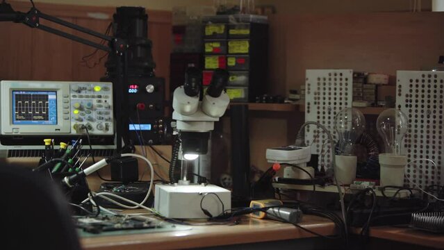 Electronics repair service workshop with soldering and diagnostics equopment. Oscilloscope, microscope and soldering iron on workspace table.