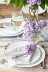 Beautiful table decor for a wedding dinner with a spring blooming lilac flowers. Celebration of a special event. Fancy white plates, wineglasses. Countryside style