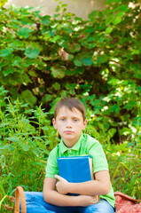 
Cute boy in a green t-shirt with a school backpack and school books in the park. Back to school