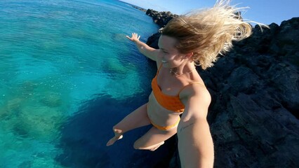 POV shot of young happy carefree woman cliff jumping into tropical blue ocean