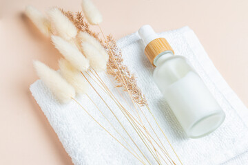 frosted glass bottle with face cream or fluid on white towl with lagurus flowers and dry reeds. Skin care eco concept. Natural cosmetics