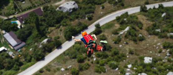 Base jumping: Basejumper figure in free fall against a blurred background with a highway and buildings below, panorama.