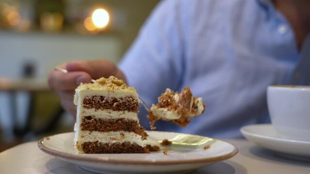 Hand of man with a fork breaks off a piece of carrot cake