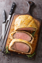 High angle beef wellington cooking or boeuf en crout cut into slices on a chopping board grey background. Vertical top view from above - obrazy, fototapety, plakaty