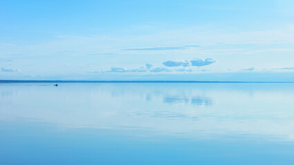 Light blue sky reflected in a calm smooth lake surface.  Summer seascape background with space for copy. Russia, Vologda Oblast, Lake Beloye. - 526436771