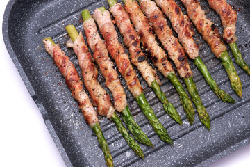 Healthy food - Asparagus wrapped with bacon and spices on grill pan isolated on white background