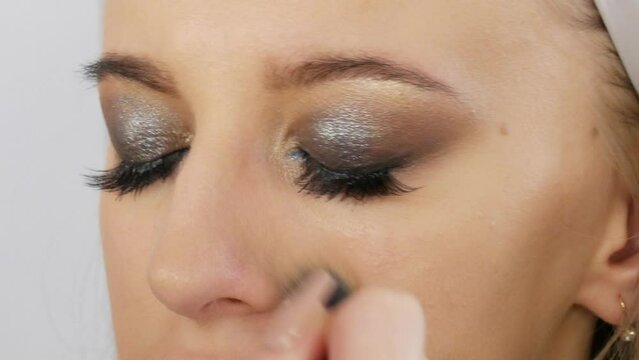 Special brush for powdering the face. A professional make-up artist makes a bright evening make-up for smoky eyes on a model with blue eyes, close-up view