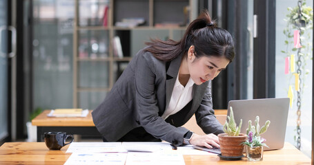 Happy attractive Asian business woman working with a laptop and financial document at office, successful action, Business concept.