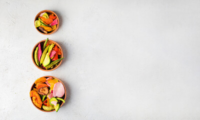 Dehydrated vegan chips crisps in wooden mango bowl. Vitamin salty free healthy fast food with carrot slices, beetroot wedges, broccoli, zucchini on a light table. food photo banner copy space top view