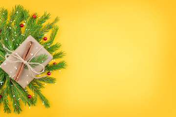 A Christmas gift in craft paper, decorated with a fir cone, cinnamon and twigs. New Year's yellow background with natural color decor. Isolated Christmas paraphernalia