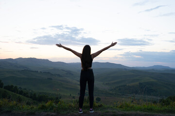 Fototapeta na wymiar girl with hands raised up in the mountains. view of the mountain valley with the silhouette of a woman