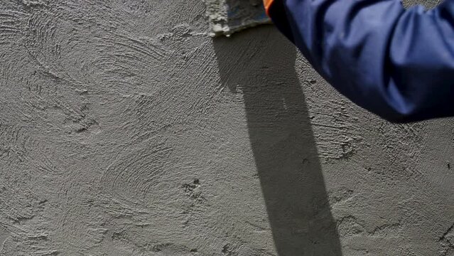 Handheld slow-motion shot of close-up construction hand workers plastering cement during the construction of the wall.