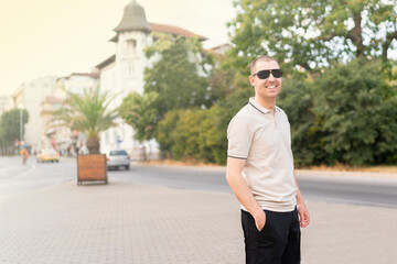Varna, Bulgaria - 15.08.22 - Young stylish man wearing t-shirt and glasses, standing on the street on city background. Street photo