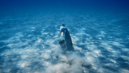 Boy snorkels with fins on the seabed raising sand smoke in the ocean