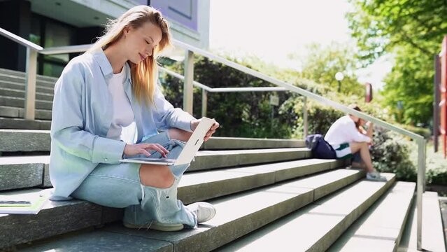 Smiling girl student using laptop computer modern technology device outdoor in university campus online learning, elearning outside sitting on urban stairs. Web education course webinars concept.