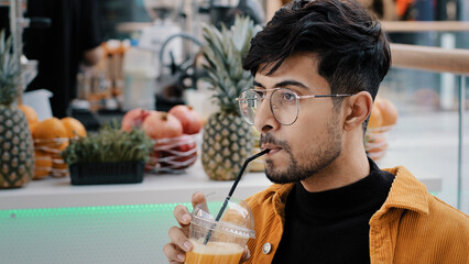 Young hispanic male cafe client resting spending weekend drinking exotic drink from plastic disposable cup relaxing happy carefree guy enjoying taste refreshing fruit juice looking at camera smiling